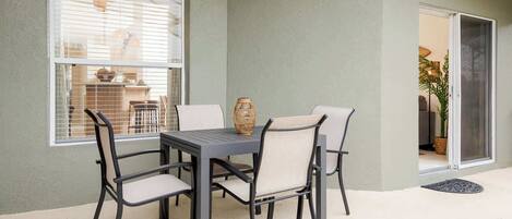 A patio with a table and chairs, a window, and a door leading to an interior space.