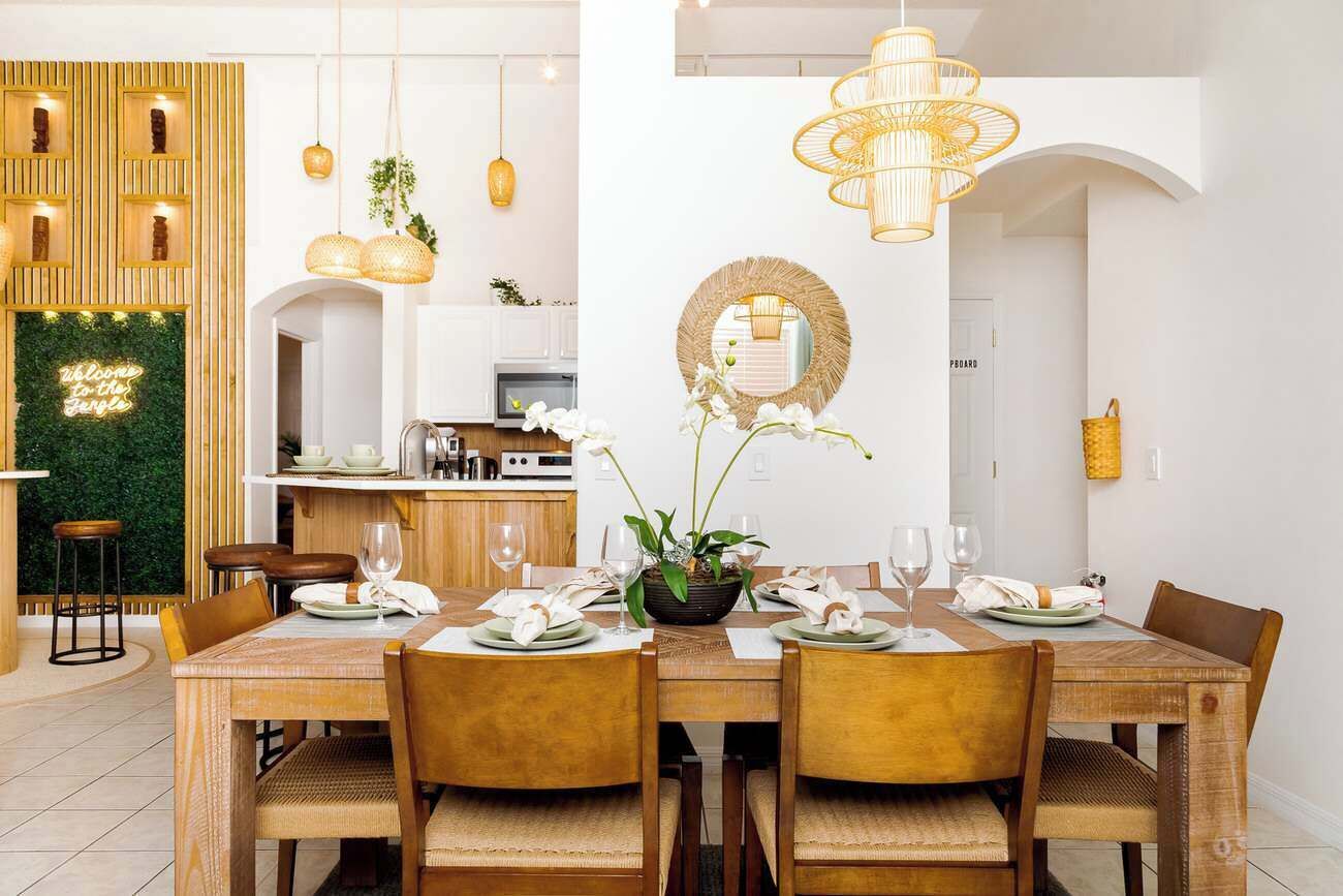 Un comedor con una mesa de madera dispuesta para cuatro personas, rodeada de sillas. Un espejo grande cuelga de la pared sobre la mesa.