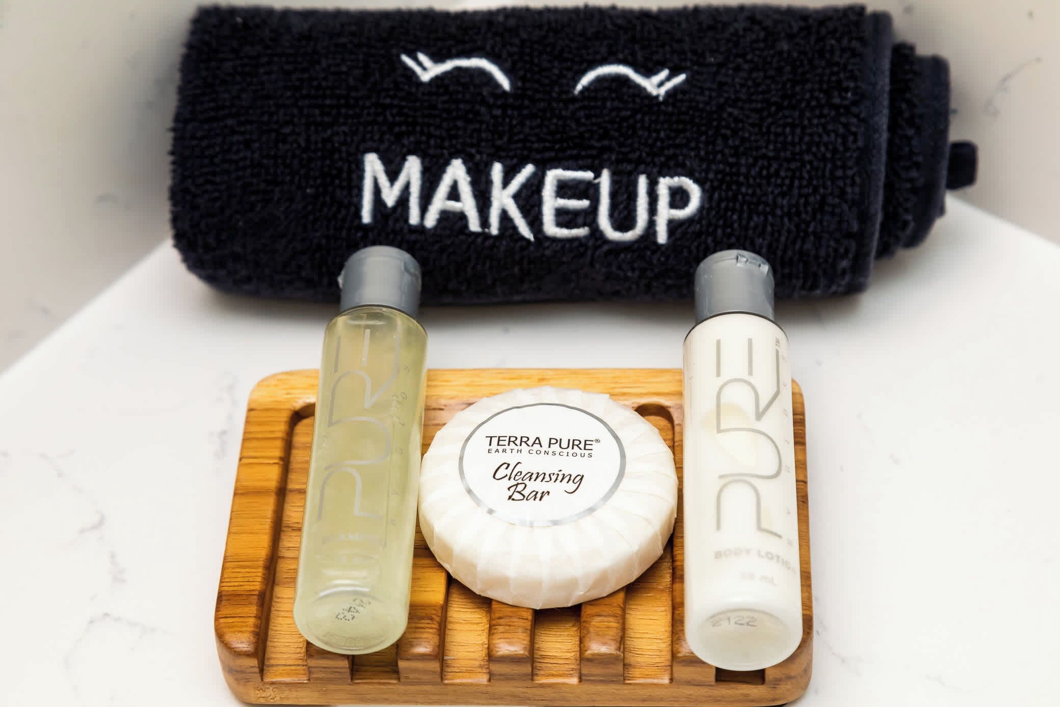 Uma bandeja de madeira com uma barra de limpeza, duas garrafas e uma toalha preta com a palavra 'MAKEUP' escrita.