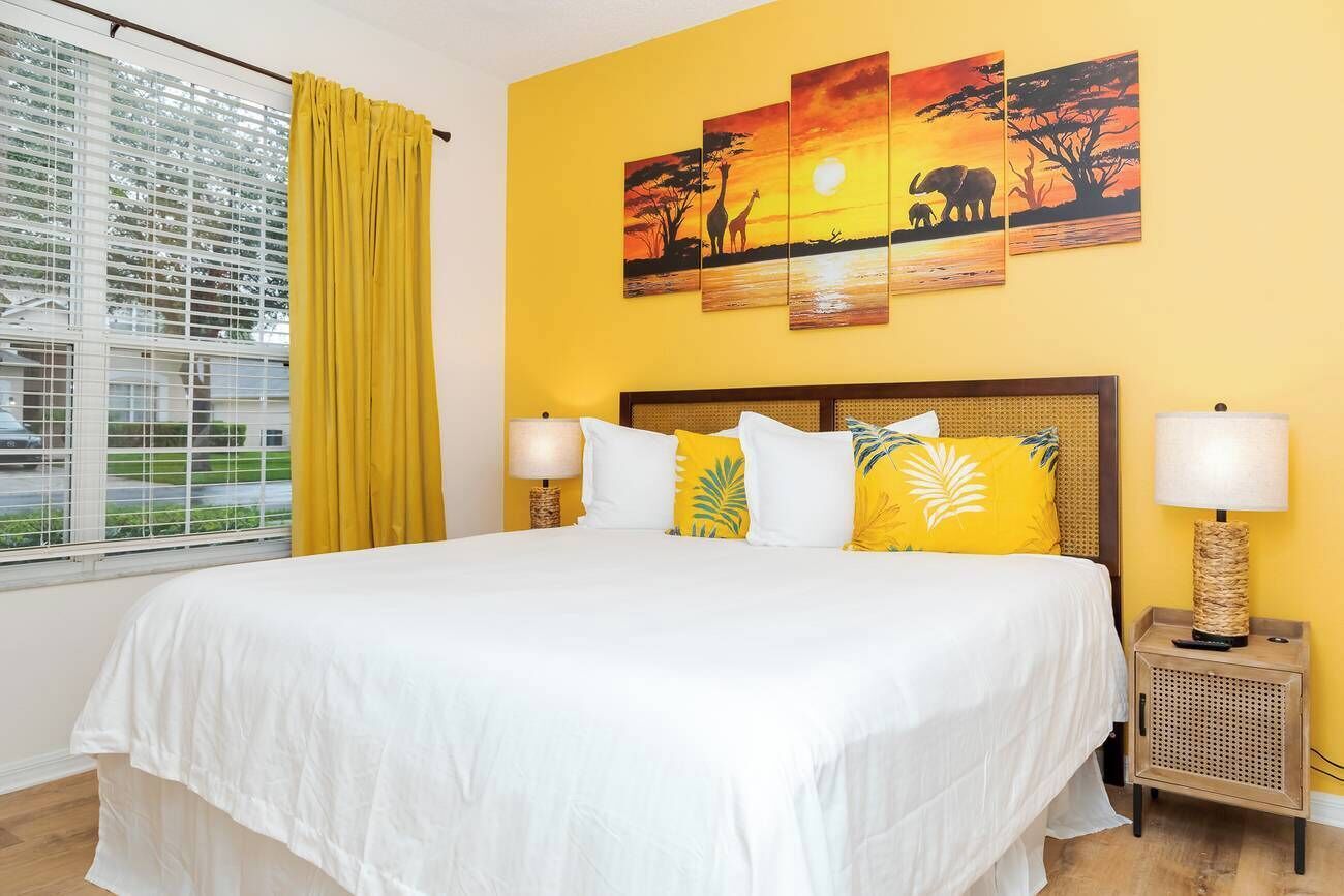 Ein Hotelzimmer mit einem großen Bett, gelben Vorhängen, einem Fenster mit Jalousien und einer Wand mit drei Wildtierbildern.