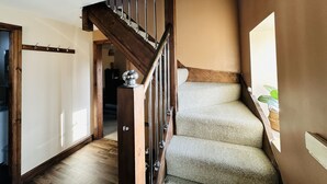 Una scala in legno con corrimano, gradini rivestiti di moquette e una porta che dà su un'altra stanza.