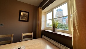 Un'area pranzo con tavolo, sedie, un quadro appeso al muro e una finestra con vista su un edificio.