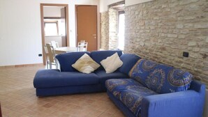Una sala de estar con un sofá azul, una mesa de comedor con sillas y una pared de piedra.