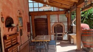 Un patio techado al aire libre con una mesa y sillas de madera, chimenea y pared de piedra.