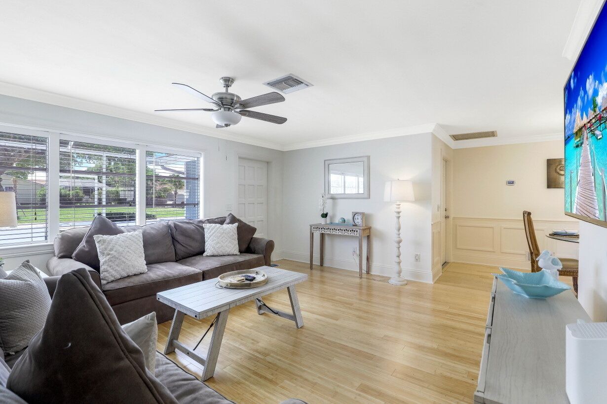 A spacious living room with a ceiling fan, a dining area with a table and chairs, and a large window offering a view of the outdoors.