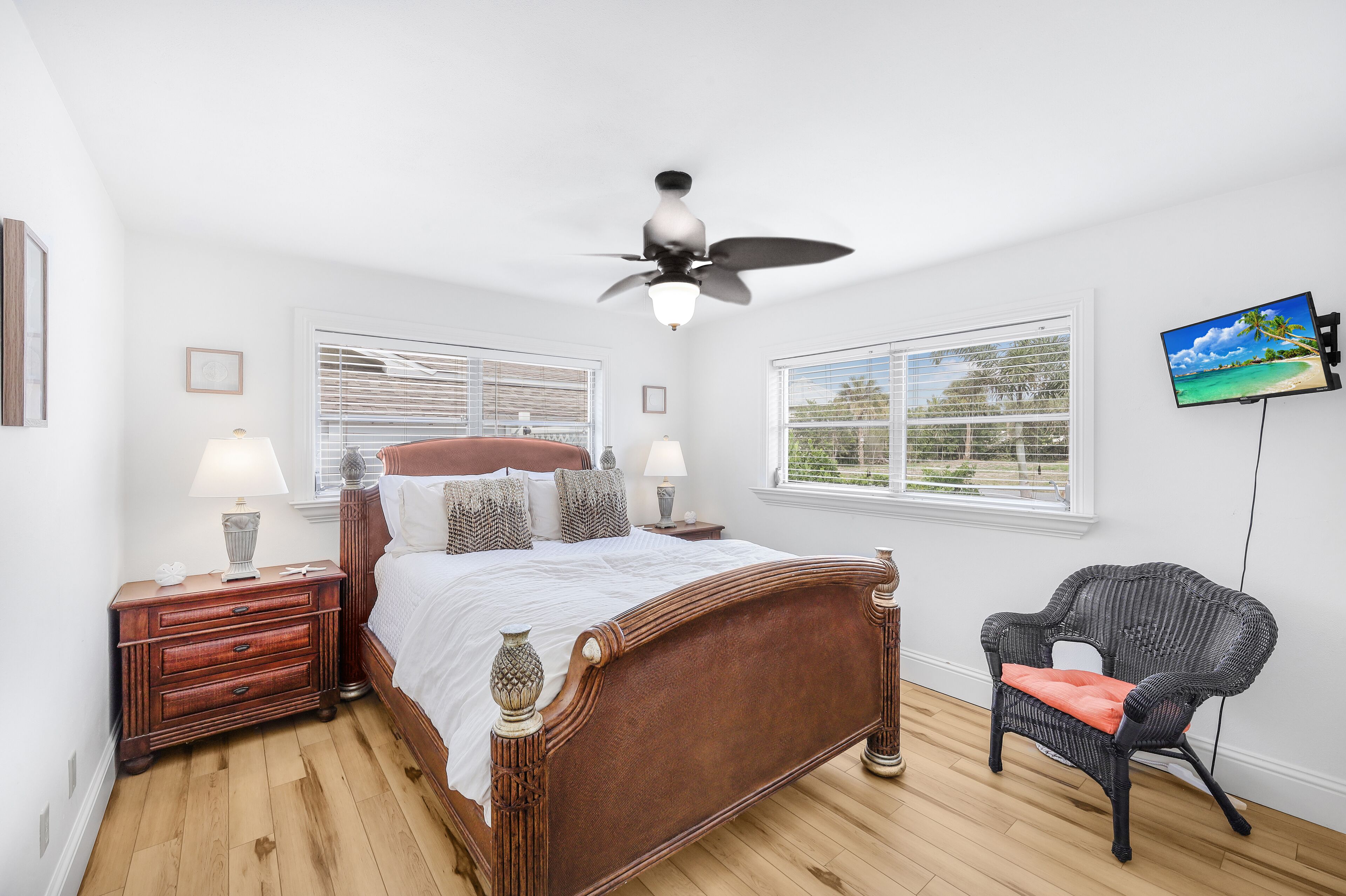A bedroom with a wooden bed, a nightstand with a lamp, a chair, and a TV on the wall.