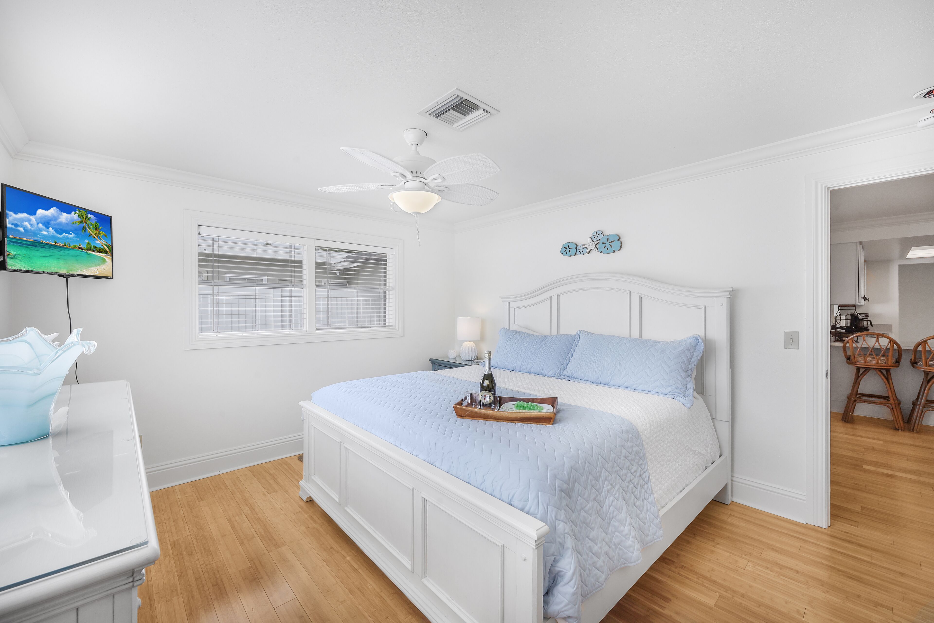 Ein Schlafzimmer mit Bett, Deckenventilator, Fernseher und Fenster mit Jalousien.