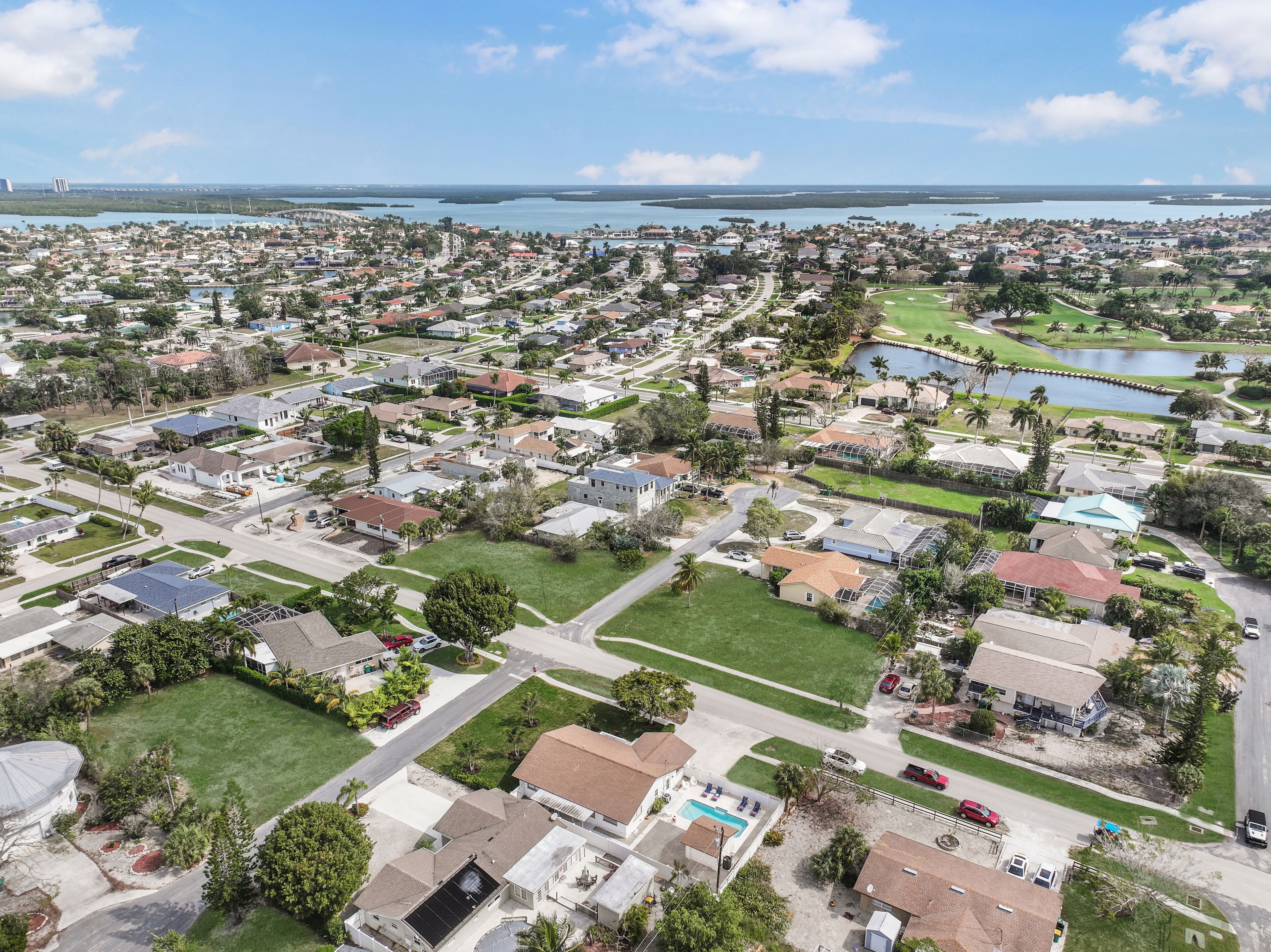 An aerial view of a residential area with houses, roads, and a large body of water in the background.