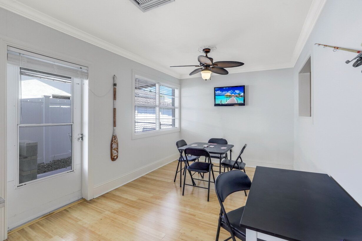Une pièce comprenant une table à manger, des chaises, un ventilateur de plafond, un téléviseur et une guitare appuyée contre le mur.