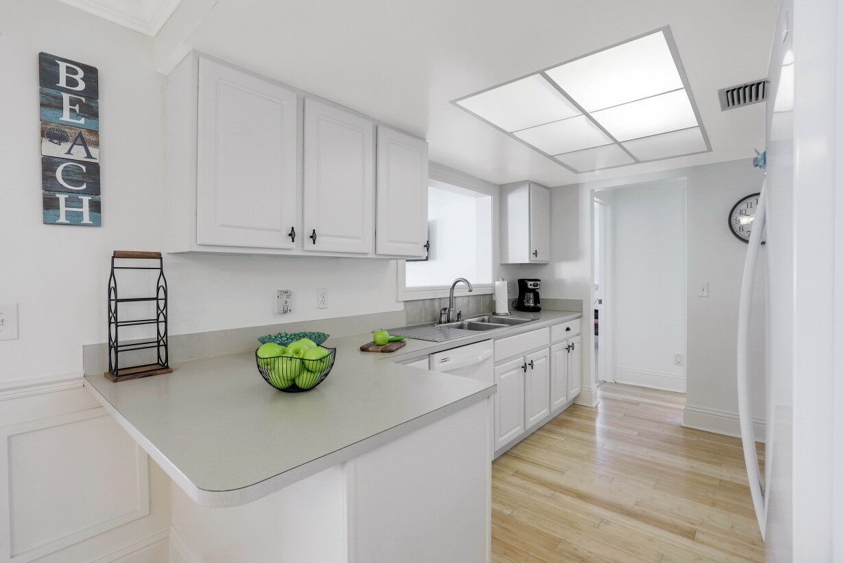 A modern kitchen with white cabinets, a large island, and a bowl of green apples.