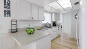 A modern kitchen with white cabinets, a large island, and a bowl of green apples. - Cozy Inland Home | Backyard & Steps to Shopping (Marco Island)