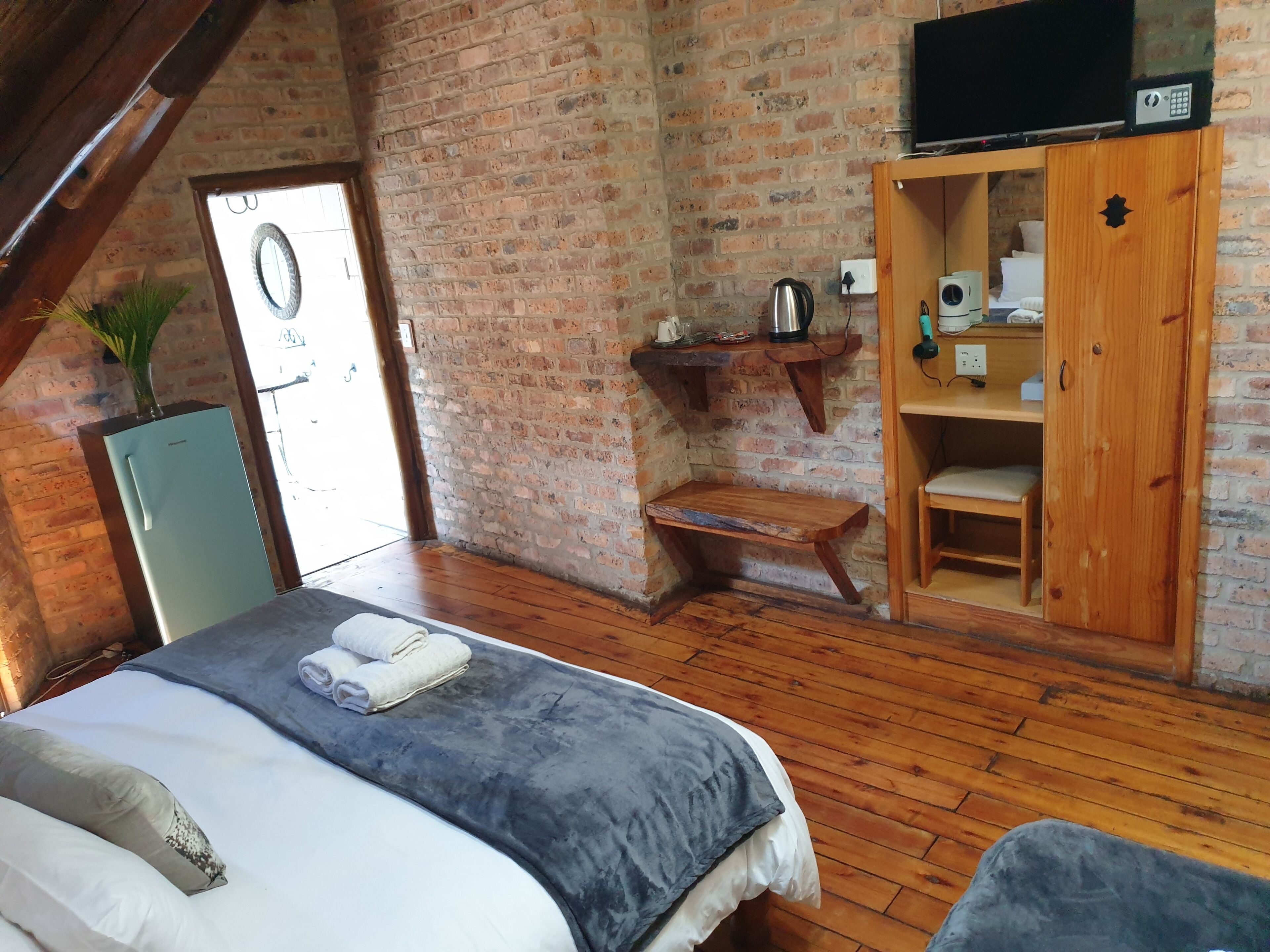 A cozy room with a bed, a wooden bench, a wardrobe, and a television mounted on the wall.