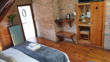 A cozy room with a bed, a wooden bench, a wardrobe, and a television mounted on the wall.