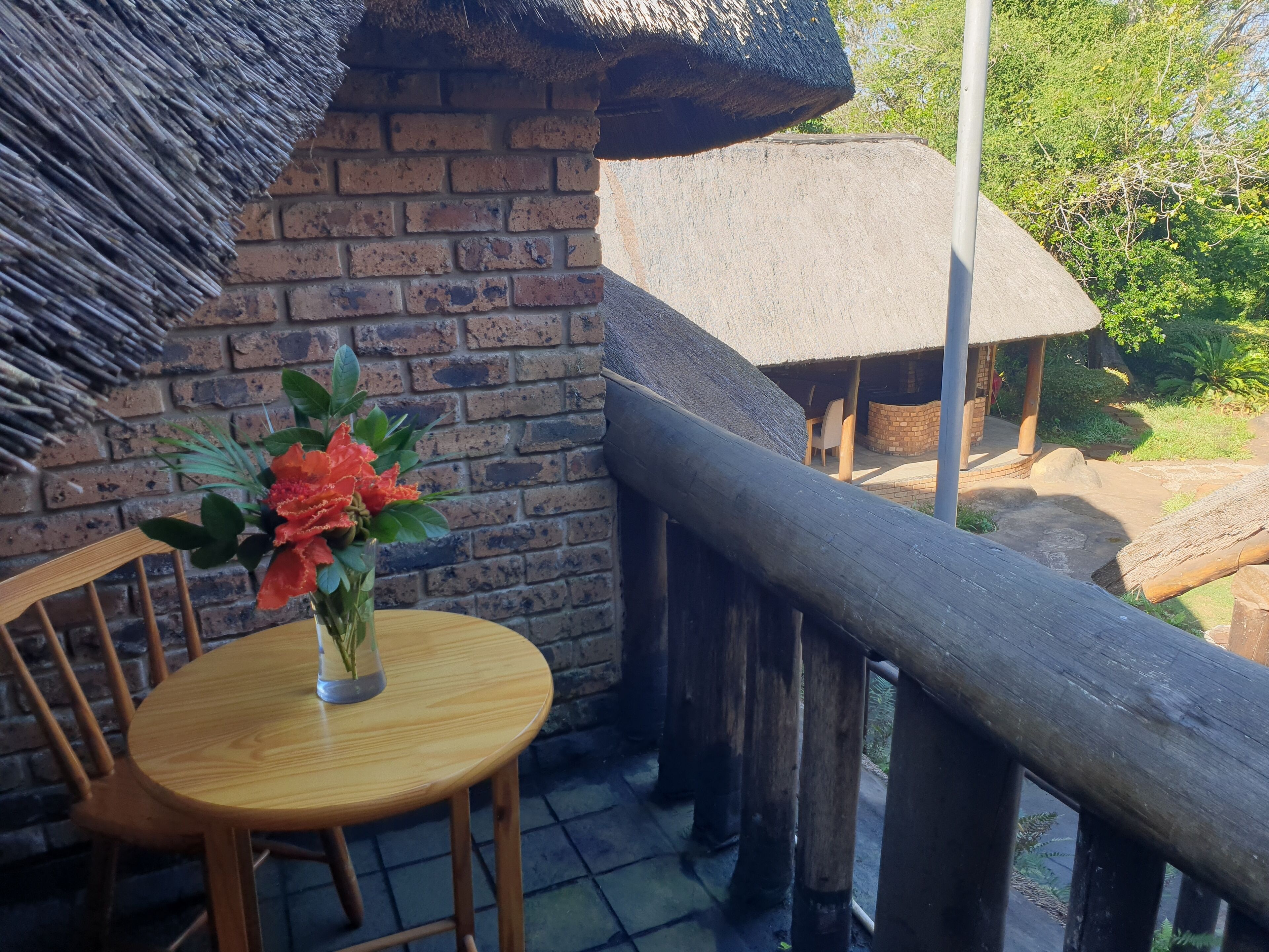 Una mesa de madera con un florero sobre un balcón con un muro de ladrillo y techo de paja.