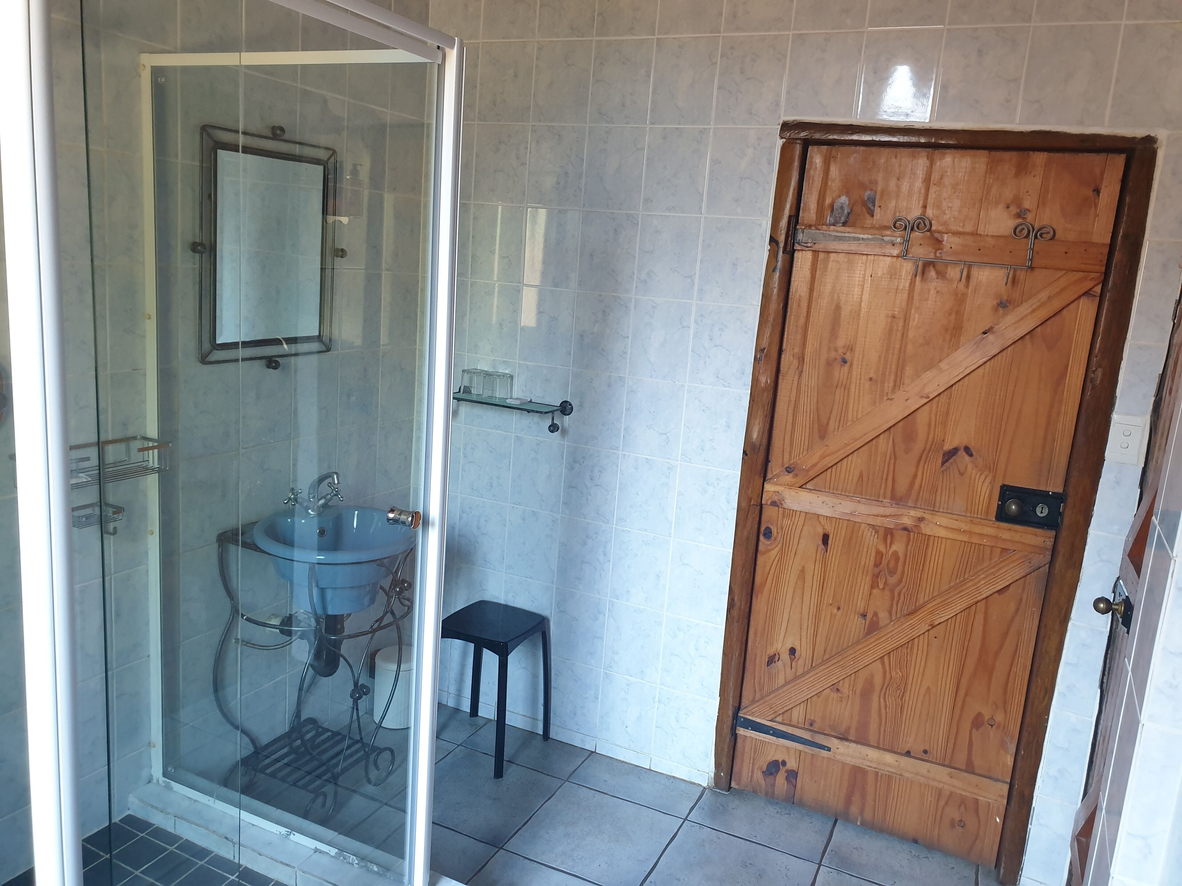 Een badkamer met een douchecabine van glas, een wastafel en een houten deur.