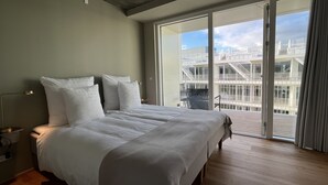 Un dormitorio moderno con una cama grande, una mesita de noche, una lámpara y vistas a un balcón con mobiliario exterior.