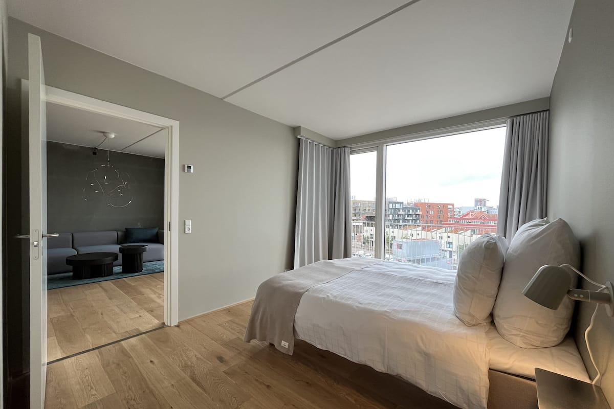 A modern bedroom with a large bed, a view of the city, and a separate seating area with a sofa and coffee table.