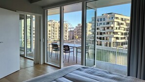Habitación de hotel moderna con una cama grande, un balcón con mesa y sillas, y vistas a la ciudad.