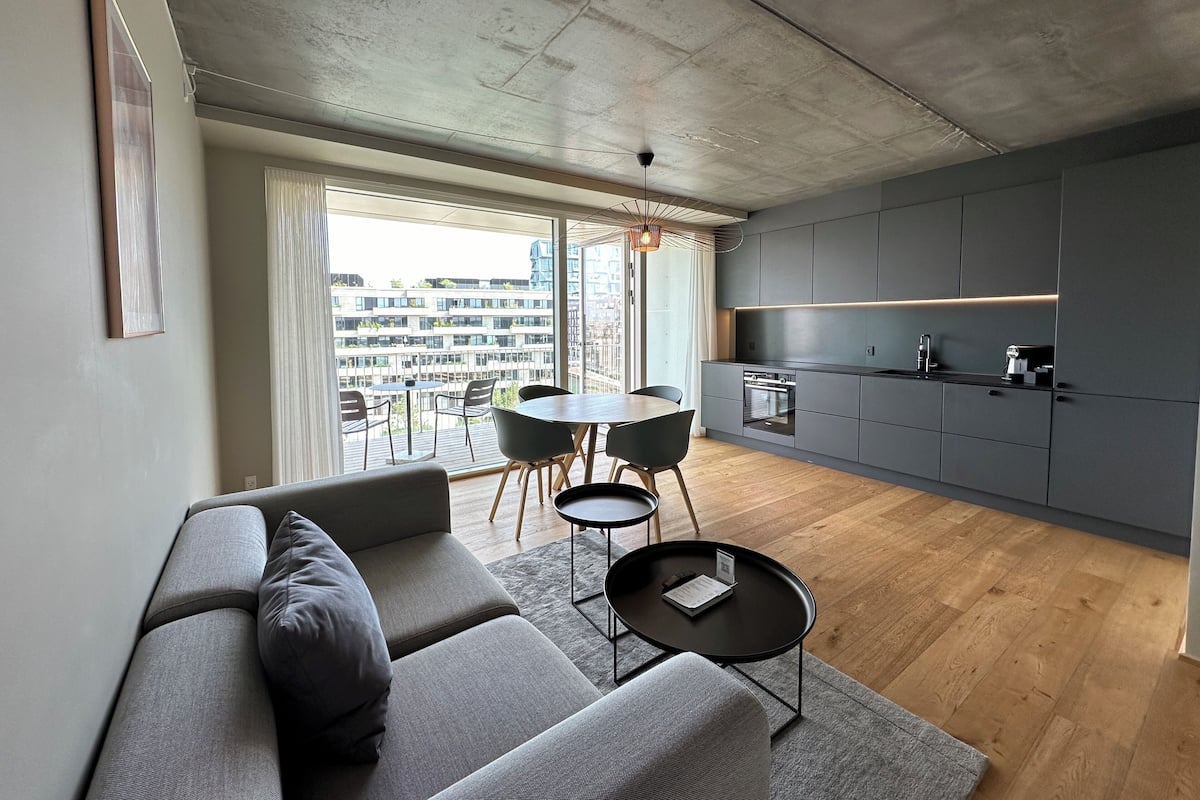 A modern living room with a grey sofa, a small round table, and a dining area with a table and chairs.