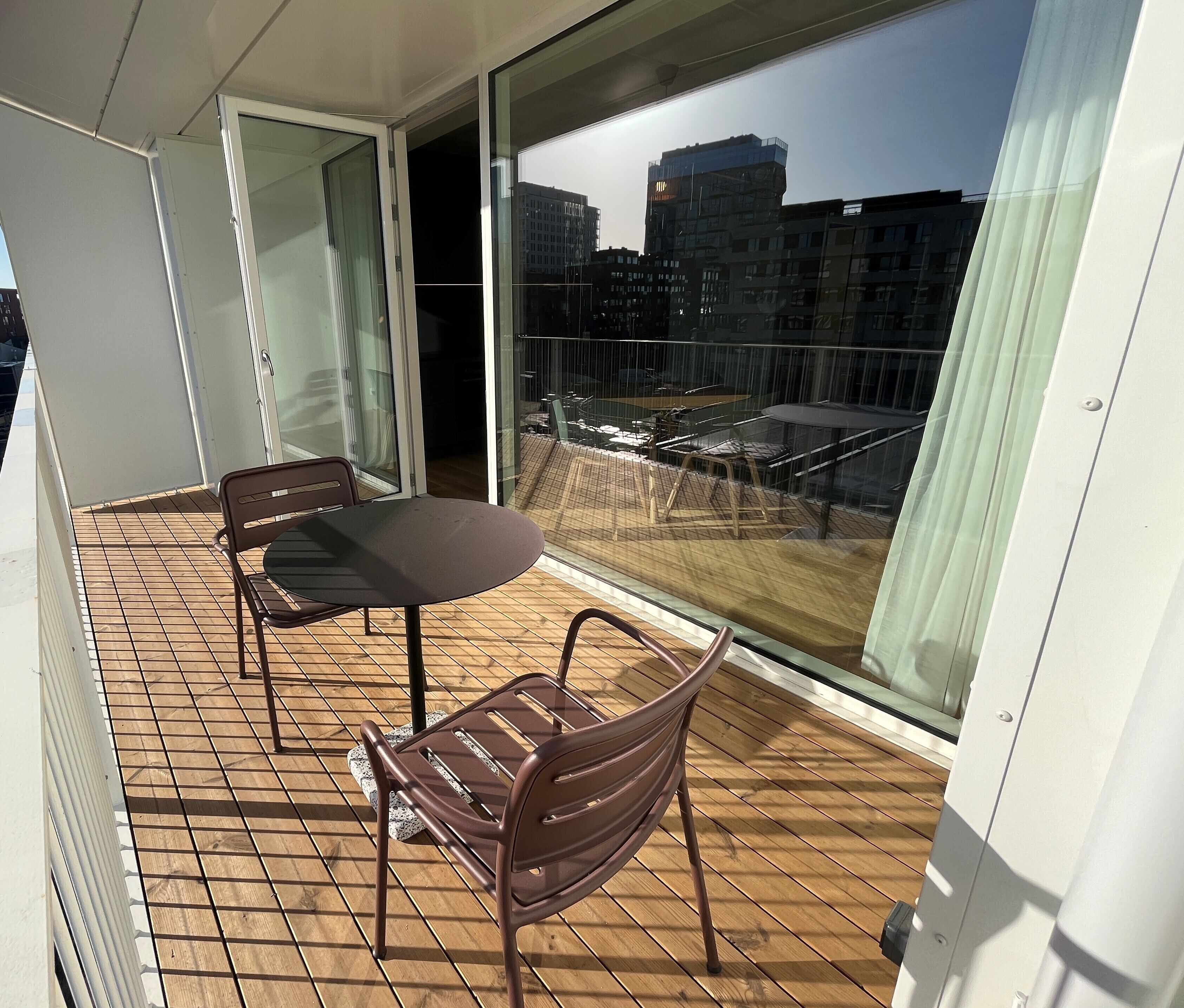 A balcony with a table and two chairs, a glass door, and a view of buildings.