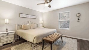 A bedroom with a bed, bedside tables, a bench, a ceiling fan, a window, and a clock on the wall. - Rockwall Duo - Cottage + Lodge Combo (Branson)
