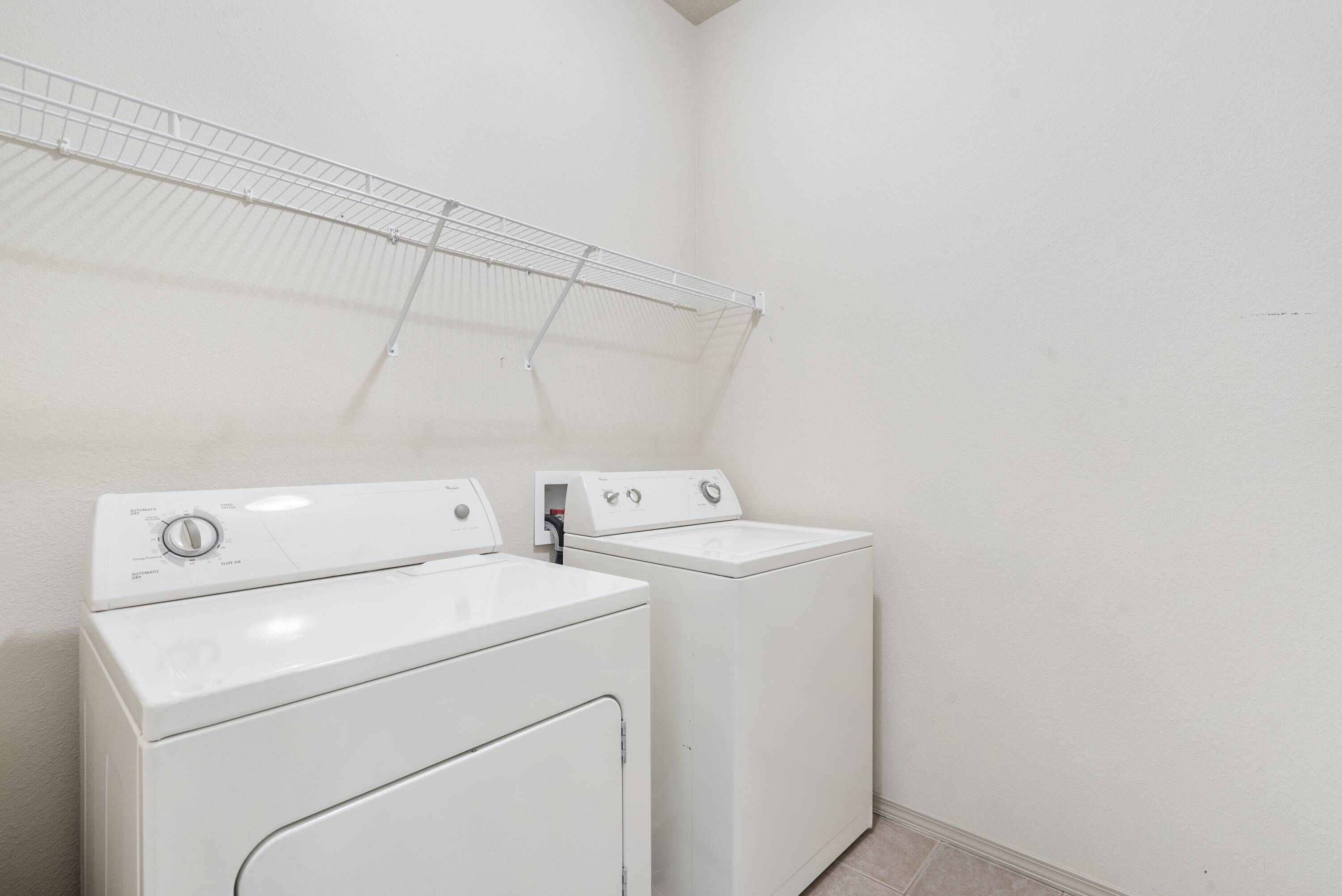 A laundry room with two white front-loading washing machines and a drying rack.