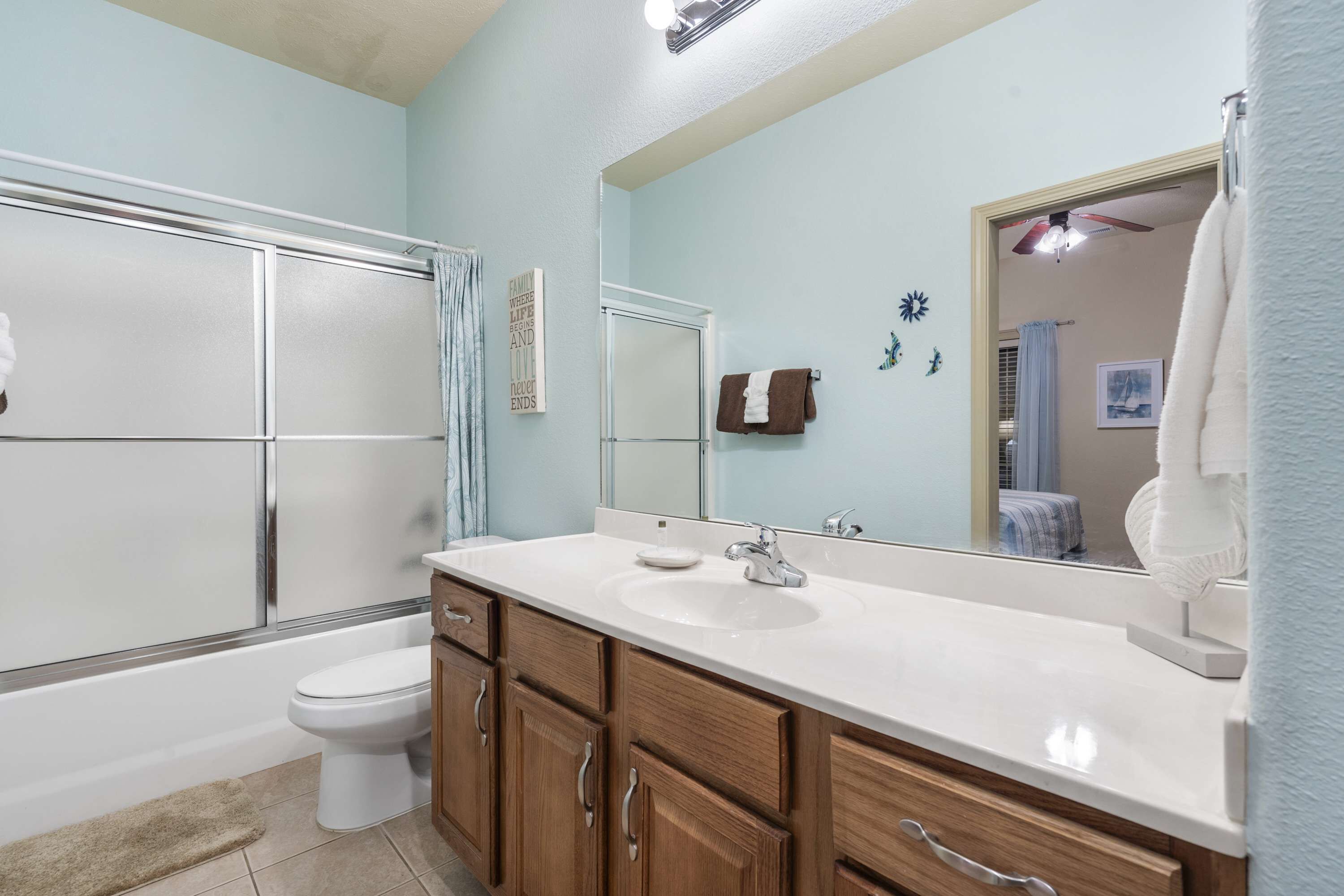 Une salle de bain avec un lavabo blanc, des meubles en bois, une cabine de douche en verre et un grand miroir.