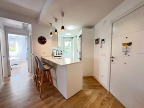 Kitchen area with central island and bar stools, featuring white cabinetry and a wooden floor.