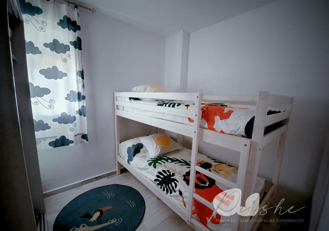 Een slaapkamer met een stapelbed, een gordijn met patroon, een rond tapijt en een wandplank.