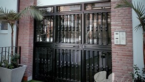Ein schwarzes Metallgitter mit dekorativem Design, in eine Ziegelwand eingelassen, oberhalb davon ein kleines Fenster.