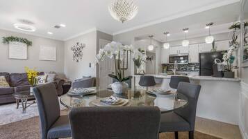 A modern kitchen with white cabinets, a black refrigerator, and a dining area with a glass table and grey chairs.