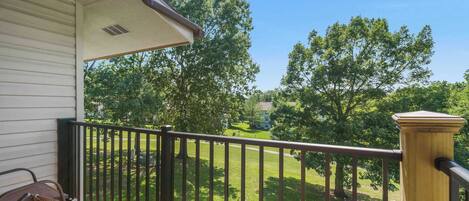 A balcony with a view of a green lawn and trees.