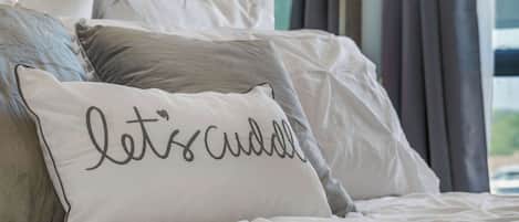 A neatly made bed with a pillow that reads "let's cuddle".