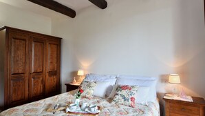Ein Schlafzimmer mit einem Bett, zwei Nachttischen, einem Holzschrank und einer blumigen Tagesdecke.