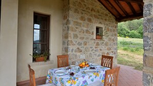 Ein Steinhaus mit überdachter Terrasse, einem gedeckten Tisch und einem Fenster mit Pflanze.