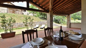 An outdoor dining area with a table set for two, a bottle of wine, and a view of the garden and hillside.