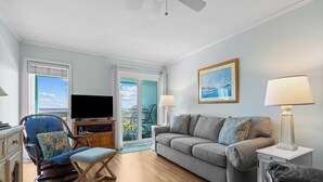 Ein Wohnzimmer mit einer Couch, einem Sessel, einem Fernseher und einem Gemälde an der Wand.