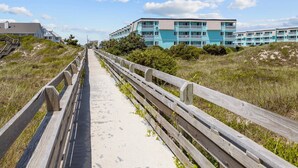 Ein Gehweg führt zu einem Strandgebäude mit mehreren Balkonen und einem Sandweg.