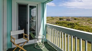 Ein Balkon mit Blick auf den Strand, ein Klappsessel und ein kleiner Tisch.
