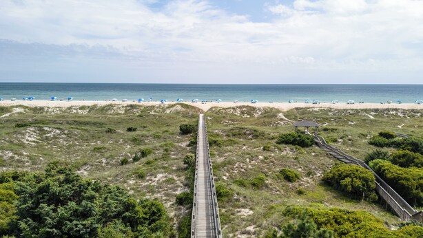Ein Strand mit einer Holzpromenade, die zum Ufer führt, feinem Sand und Strandliegen.