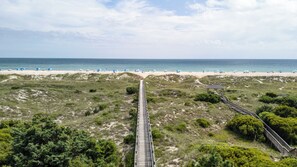 A beach with a wooden boardwalk leading to the shore, sandy beach, and beach umbrellas.
