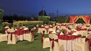 An outdoor event space with round tables and chairs, decorated with red and white linens. - Yashail Hotel Haridwar (Haridwar)