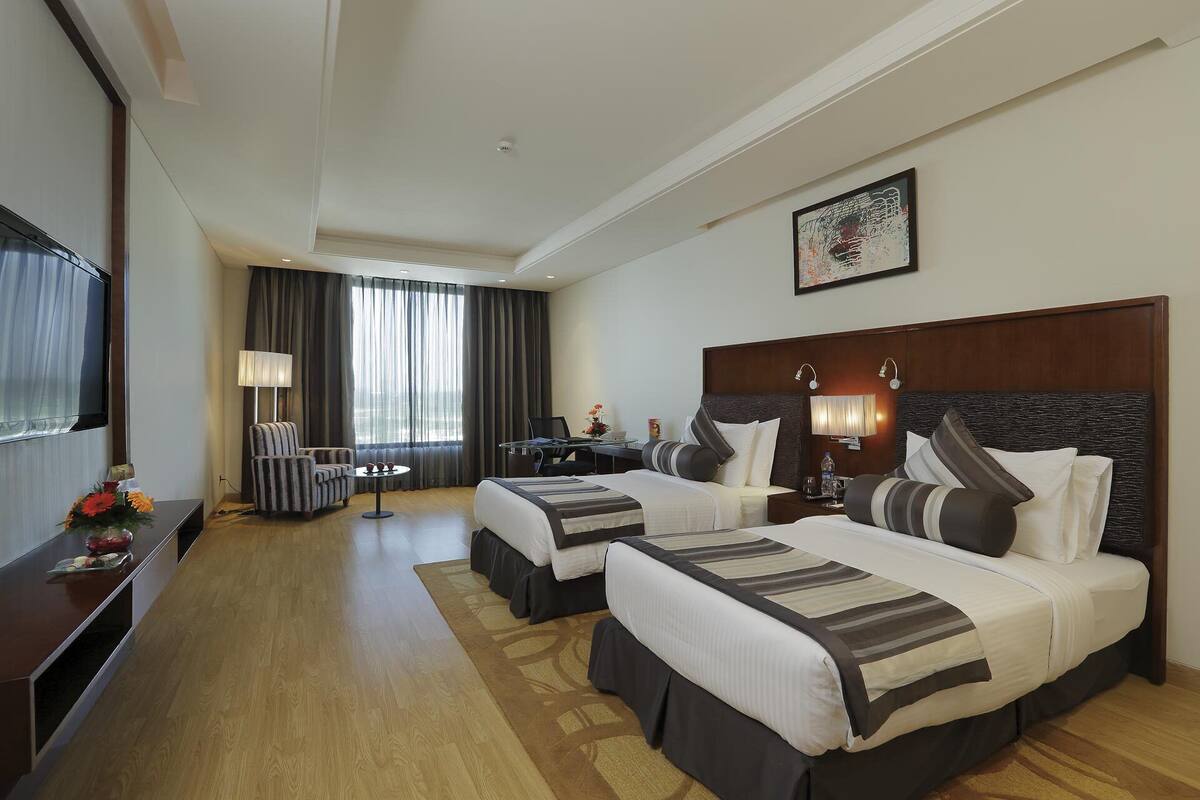 Habitación de hotel con dos camas, un escritorio, una silla, un televisor y un ventanal con cortinas.