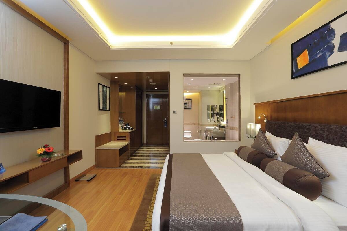 Habitación de hotel moderna con una cama grande, un televisor de pantalla plana, un escritorio y un baño visible a través de una puerta abierta.