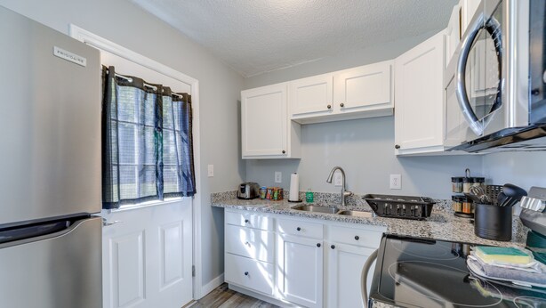 A kitchen with white cabinets, a stainless steel refrigerator, a microwave, and a sink.