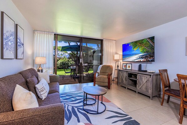 A living room with a sofa, armchair, coffee table, and a flat-screen TV mounted on the wall.