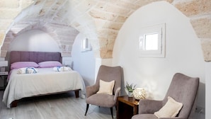 Quarto com uma cama, duas poltronas, uma mesa de cabeceira e uma mesinha com abajur.
