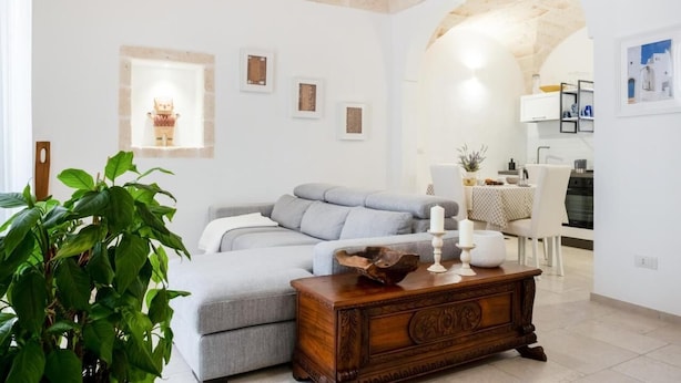 Uma sala de estar moderna com um sofá cinzento, uma mesa lateral de madeira e uma grande planta verde.