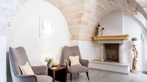 Um quarto acolhedor com duas poltronas cinzentas, uma mesinha com uma planta, lareira e uma parede de pedra.