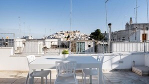 Terraço no telhado com mesa e cadeiras, com vista para uma cidade histórica com edifícios e uma colina ao fundo.